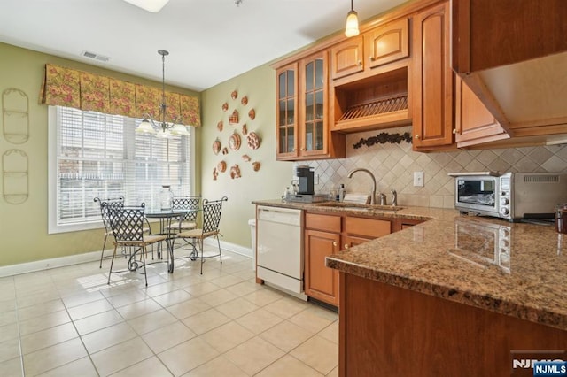 kitchen featuring visible vents, white dishwasher, a sink, hanging light fixtures, and tasteful backsplash