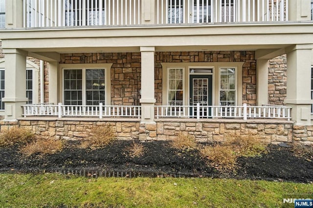 entrance to property featuring stone siding, a porch, and a balcony