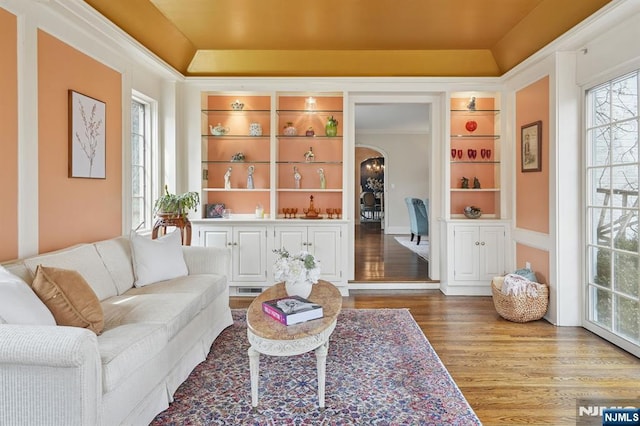 living room featuring built in shelves, a tray ceiling, arched walkways, and wood finished floors