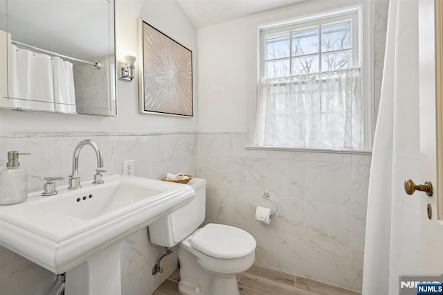 full bath with a wainscoted wall, toilet, a sink, wood finished floors, and tile walls