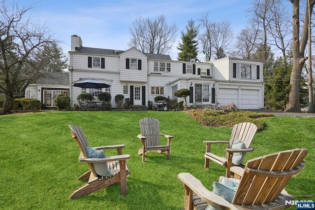 back of house with a fire pit, aphalt driveway, a lawn, a chimney, and a garage