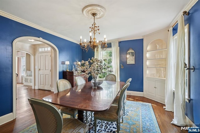 dining area with wood finished floors, baseboards, arched walkways, crown molding, and a notable chandelier