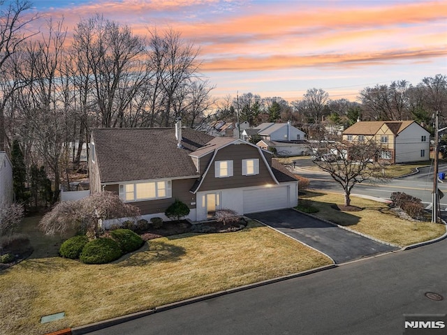 view of front of house featuring a gambrel roof, driveway, a yard, a shingled roof, and a chimney