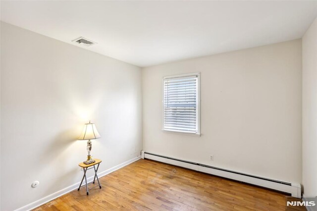 spare room with baseboard heating, baseboards, visible vents, and wood finished floors