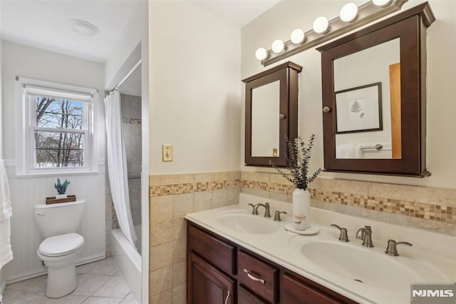 full bath with a sink, toilet, wainscoting, and tile patterned flooring