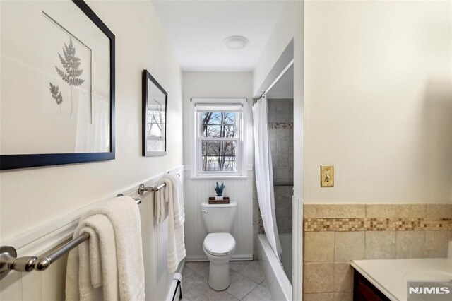 full bath with vanity, a wainscoted wall, tile patterned flooring, shower / bath combo with shower curtain, and toilet