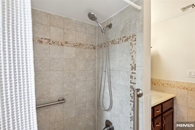 bathroom with visible vents, tiled shower, tile walls, and vanity