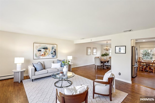 living area featuring a notable chandelier, wood finished floors, visible vents, and baseboards