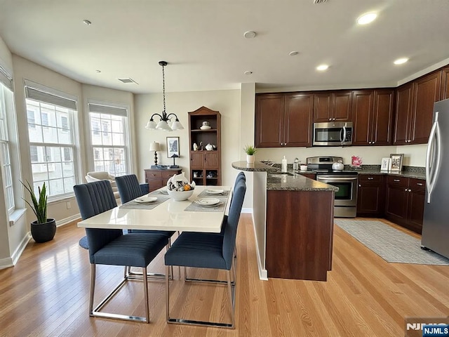 kitchen featuring light wood finished floors, a notable chandelier, appliances with stainless steel finishes, and a breakfast bar area