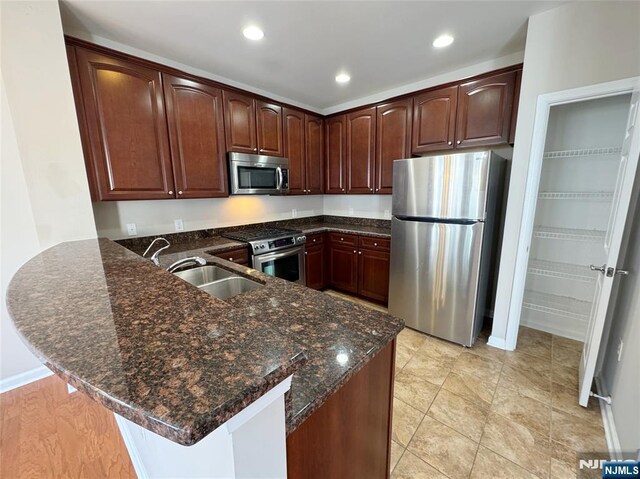 kitchen featuring a peninsula, dark stone countertops, appliances with stainless steel finishes, and a sink