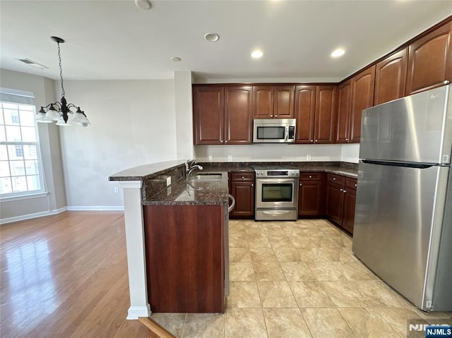 kitchen with visible vents, a peninsula, dark stone counters, a sink, and appliances with stainless steel finishes