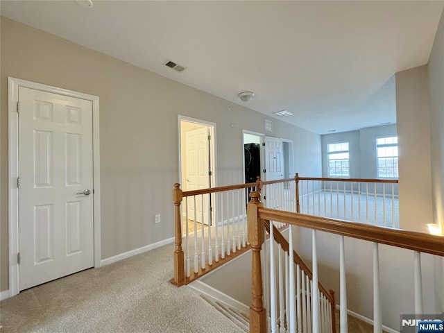 corridor with baseboards, an upstairs landing, visible vents, and carpet flooring