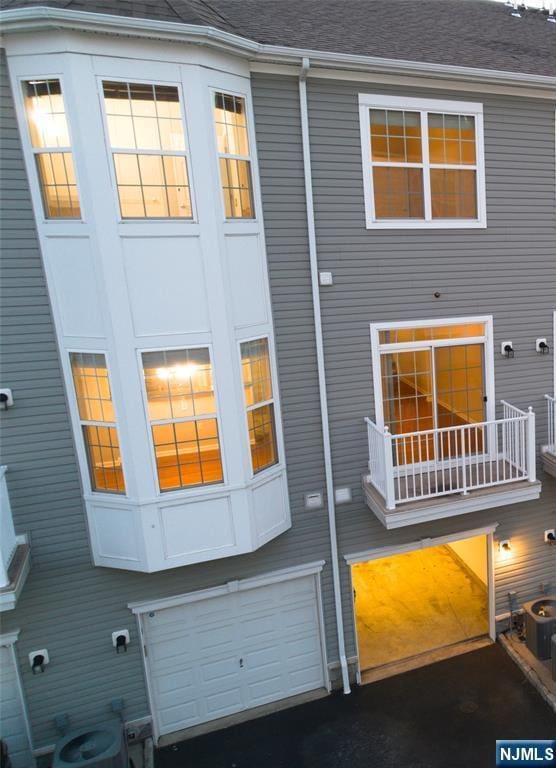 rear view of property featuring an attached garage, central AC unit, and roof with shingles