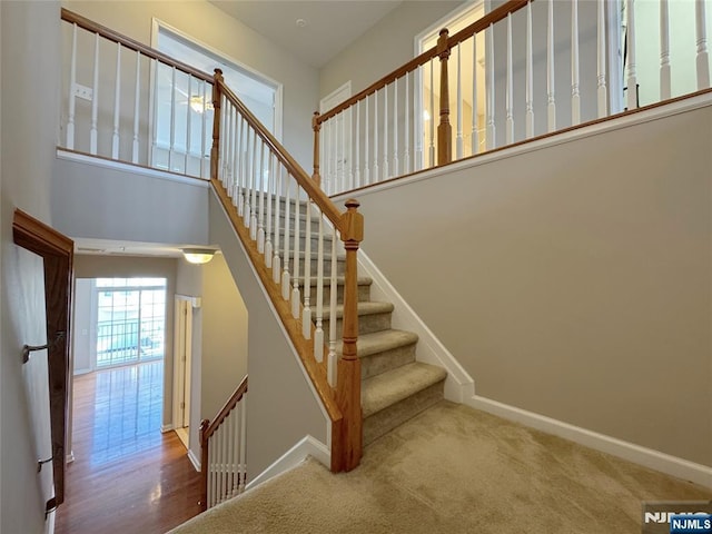 stairway featuring baseboards, a high ceiling, and carpet floors