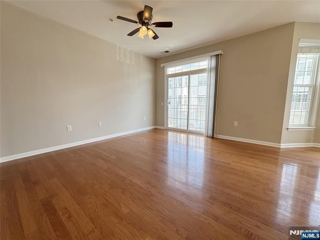 empty room with a ceiling fan, plenty of natural light, wood finished floors, and baseboards