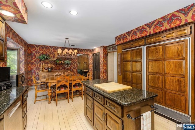 kitchen featuring a notable chandelier, a kitchen island, dark stone counters, light wood-style floors, and wallpapered walls