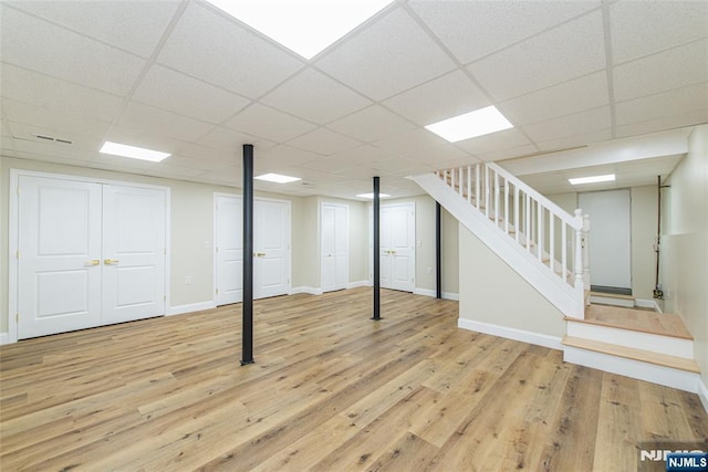 finished basement featuring a drop ceiling, stairway, baseboards, and wood finished floors