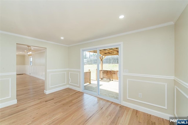 empty room with crown molding, a decorative wall, light wood-type flooring, and wainscoting