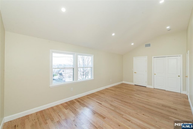 empty room with visible vents, lofted ceiling, light wood-type flooring, and baseboards