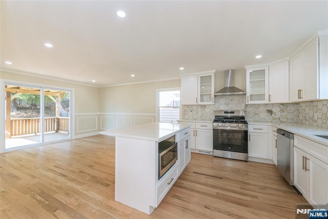 kitchen featuring light wood-style flooring, stainless steel appliances, light countertops, wall chimney exhaust hood, and backsplash