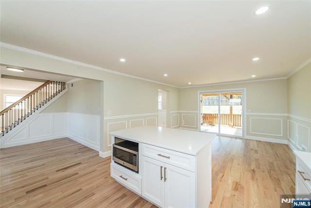 kitchen with stainless steel microwave, white cabinets, light countertops, and light wood-style floors