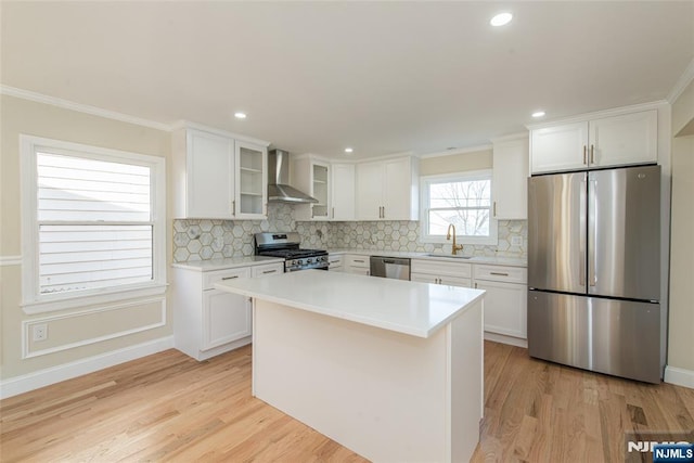 kitchen with light wood-style flooring, a sink, stainless steel appliances, white cabinetry, and wall chimney range hood