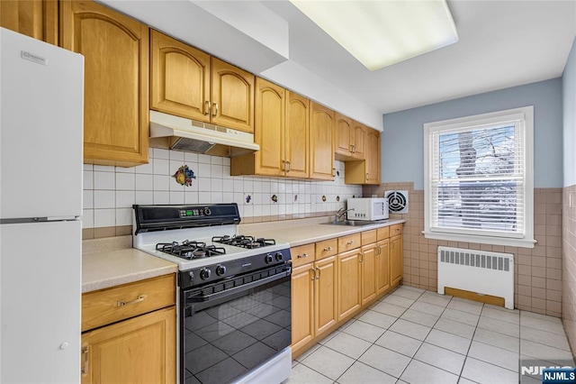 kitchen featuring under cabinet range hood, white appliances, radiator, light countertops, and light tile patterned floors