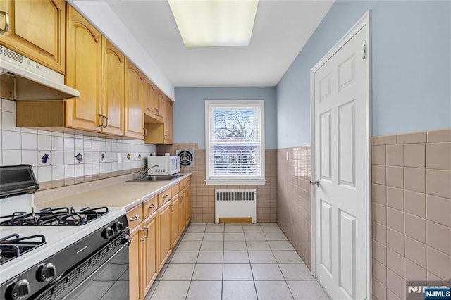 kitchen featuring radiator, gas stove, light tile patterned flooring, light countertops, and under cabinet range hood