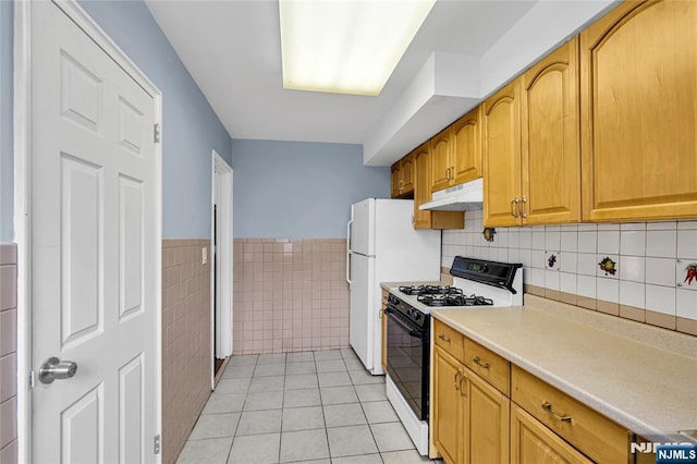 kitchen featuring range with gas stovetop, a wainscoted wall, light tile patterned flooring, light countertops, and under cabinet range hood