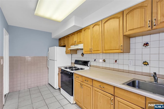 kitchen with under cabinet range hood, gas range, light countertops, light tile patterned floors, and a sink