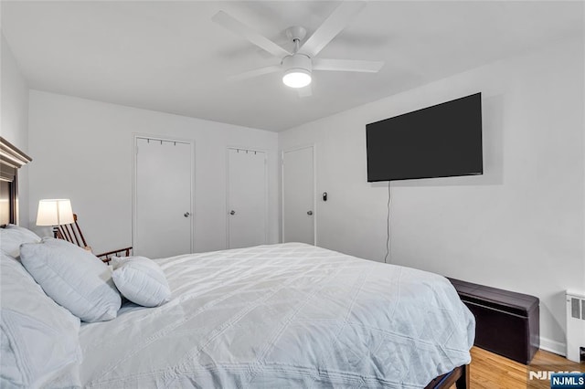 bedroom featuring light wood-style flooring, radiator heating unit, two closets, and ceiling fan