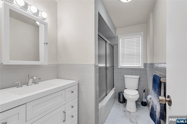 bathroom with toilet, vanity, combined bath / shower with glass door, marble finish floor, and tile walls