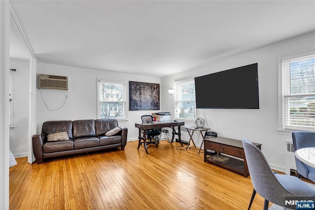 living area featuring baseboards, light wood finished floors, and a wall mounted AC