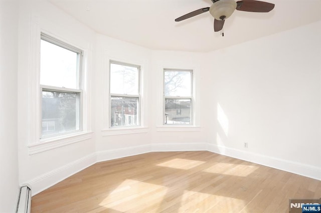 spare room featuring a baseboard heating unit, baseboards, light wood-style floors, and ceiling fan