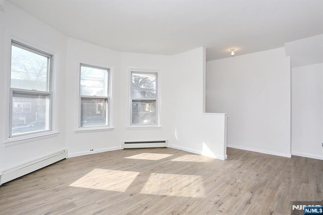 spare room featuring a baseboard heating unit, baseboards, baseboard heating, and wood finished floors