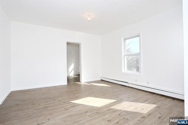 empty room with a baseboard heating unit, baseboards, and wood finished floors