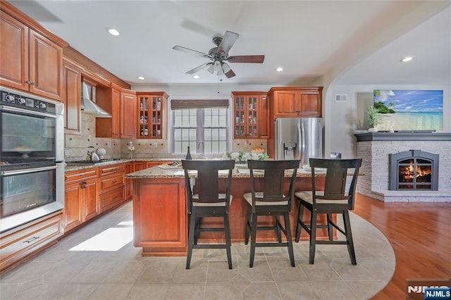 kitchen featuring a kitchen bar, a kitchen island, stainless steel appliances, wall chimney exhaust hood, and decorative backsplash