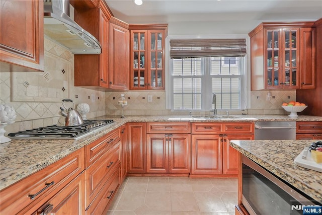 kitchen with light stone counters, appliances with stainless steel finishes, wall chimney exhaust hood, and a sink