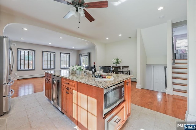 kitchen with a wealth of natural light, light stone counters, appliances with stainless steel finishes, and a baseboard radiator