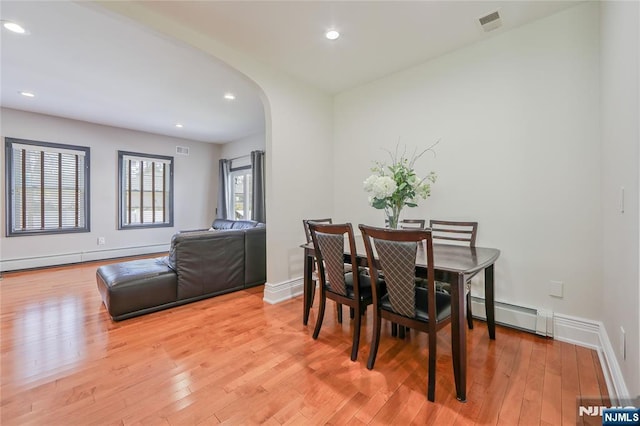 dining area with arched walkways, visible vents, light wood-style flooring, and a baseboard heating unit