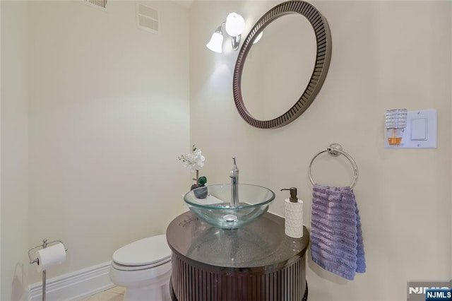 half bath featuring toilet, baseboards, visible vents, and a sink