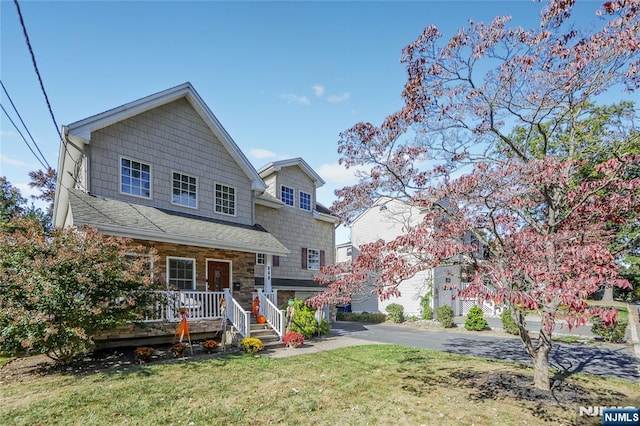 view of front of property featuring aphalt driveway, stone siding, covered porch, and a front yard