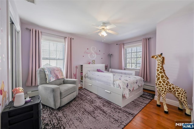 bedroom featuring a baseboard heating unit, multiple windows, and wood finished floors