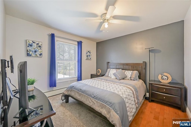 bedroom with light wood finished floors, a baseboard heating unit, and a ceiling fan