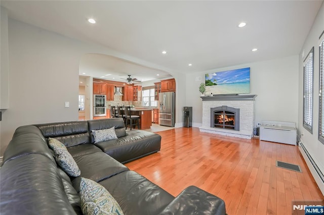 living area with arched walkways, visible vents, light wood-type flooring, and a baseboard heating unit