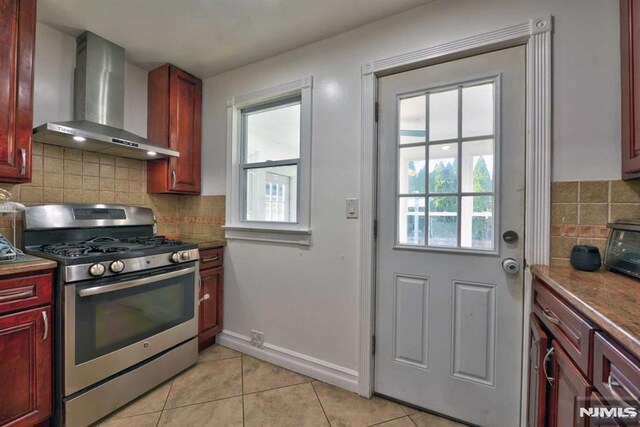 kitchen with light tile patterned floors, wall chimney exhaust hood, stainless steel range with gas cooktop, and dark brown cabinets