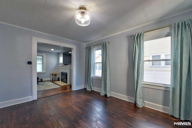 unfurnished room featuring a fireplace with flush hearth, ornamental molding, baseboards, and wood finished floors