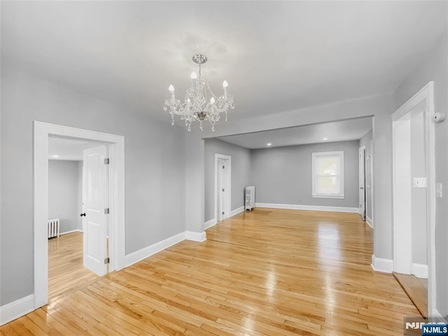 unfurnished living room featuring an inviting chandelier, radiator heating unit, baseboards, and light wood finished floors