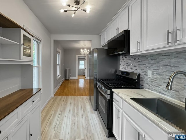 kitchen with stainless steel range with gas cooktop, a sink, light wood-type flooring, backsplash, and a chandelier