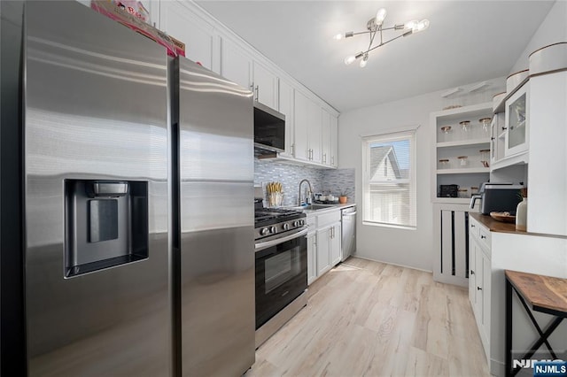 kitchen featuring light wood-type flooring, backsplash, appliances with stainless steel finishes, and white cabinetry